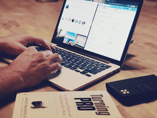 Man typing on Laptop with book and phone on wood table